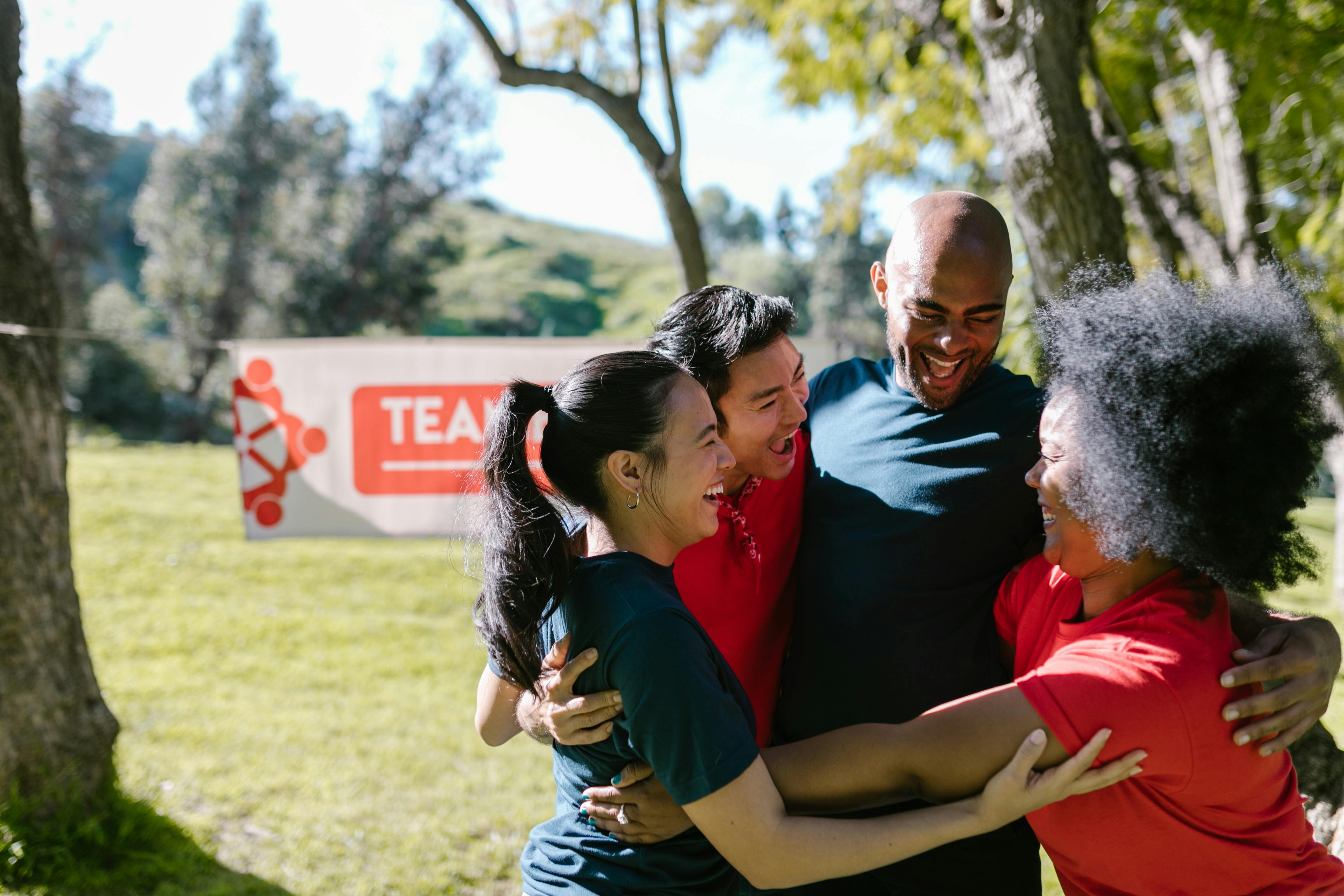 Un groupe uni en plein air, bras dessus bras dessous devant une banderole "TEAM", partageant un moment fort après un effort collectif, probablement sportif