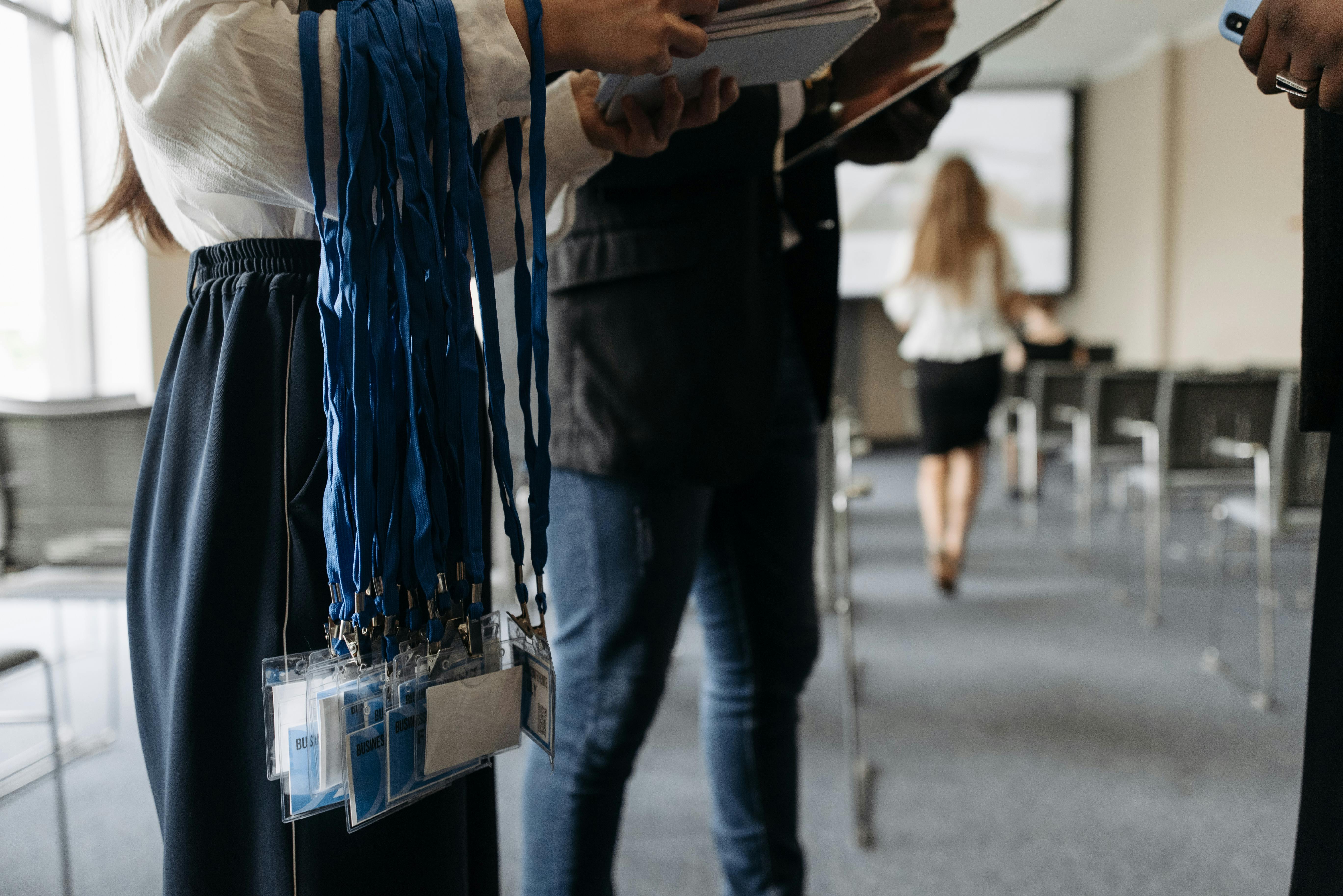 Deux personnes préparent un événement d’entreprise, distribuant des feuilles et tenant des badges, avec des chaises et un écran en arrière-plan