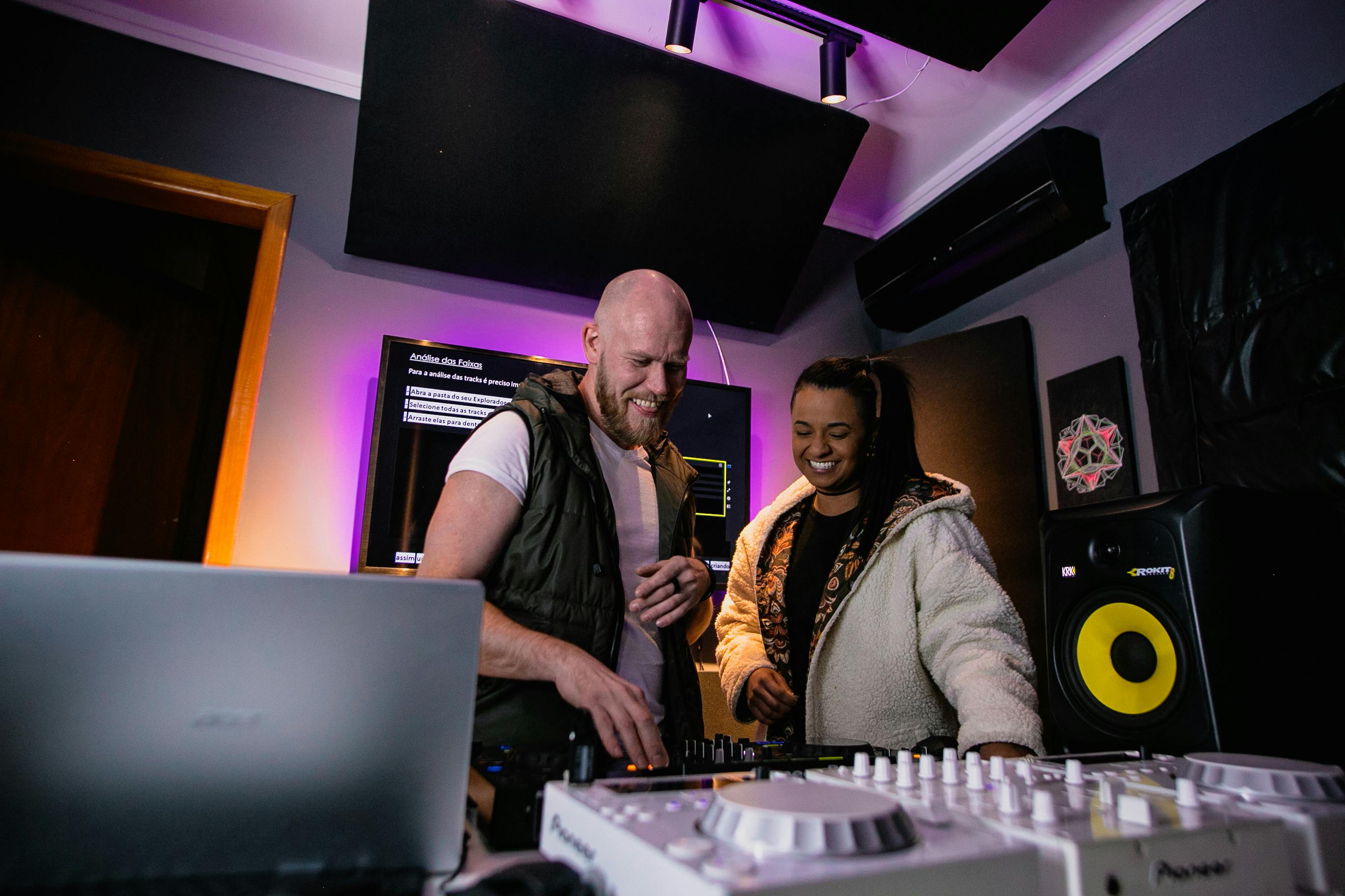 Deux personnes souriantes collaborant ensemble sur une table de mixage lors de la préparation d’un projet musical