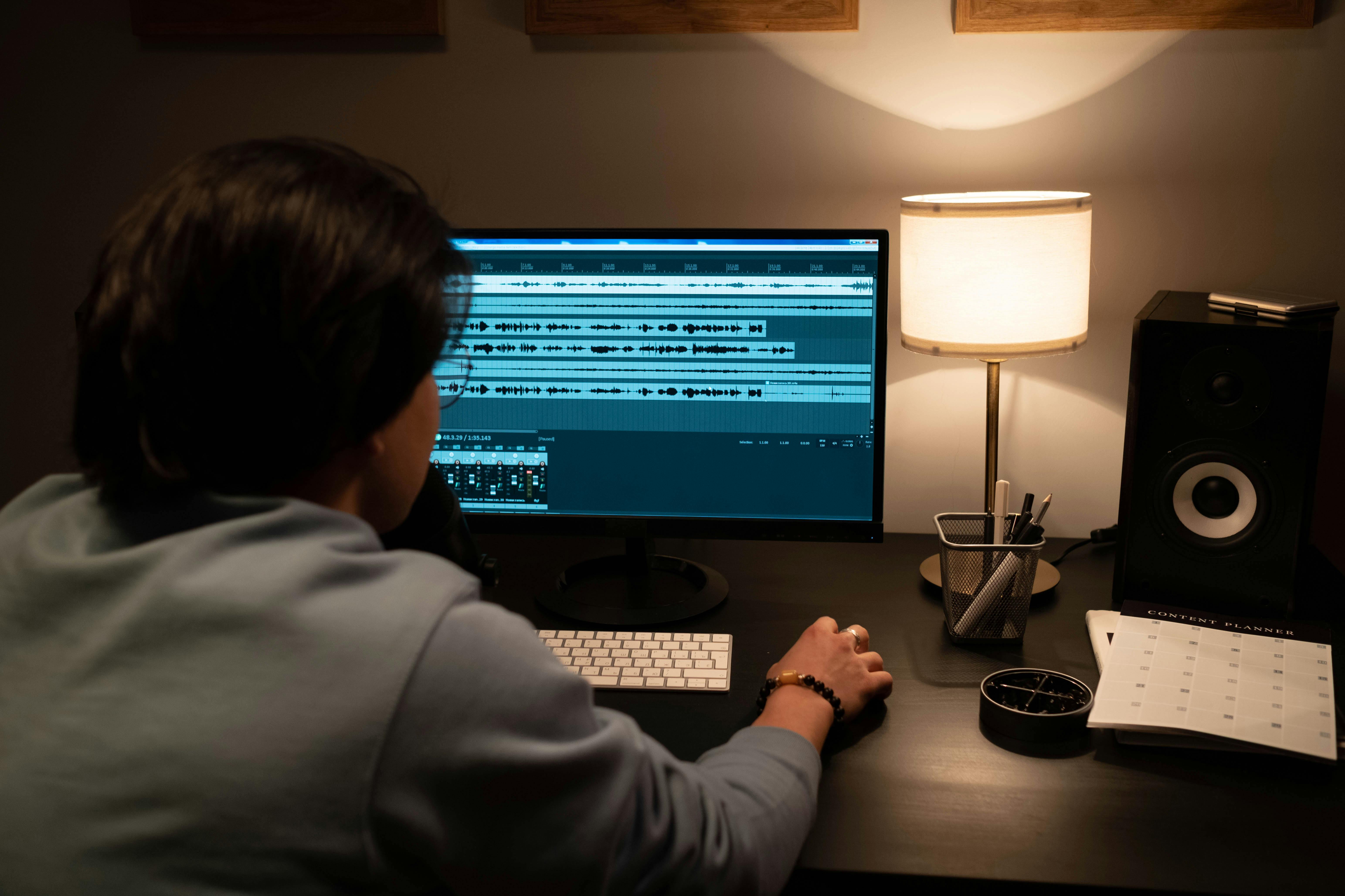Une personne concentrée devant un ordinateur affichant un logiciel de production musicale, avec un planning papier posé à côté, combinant créativité et rigueur dans son processus de composition