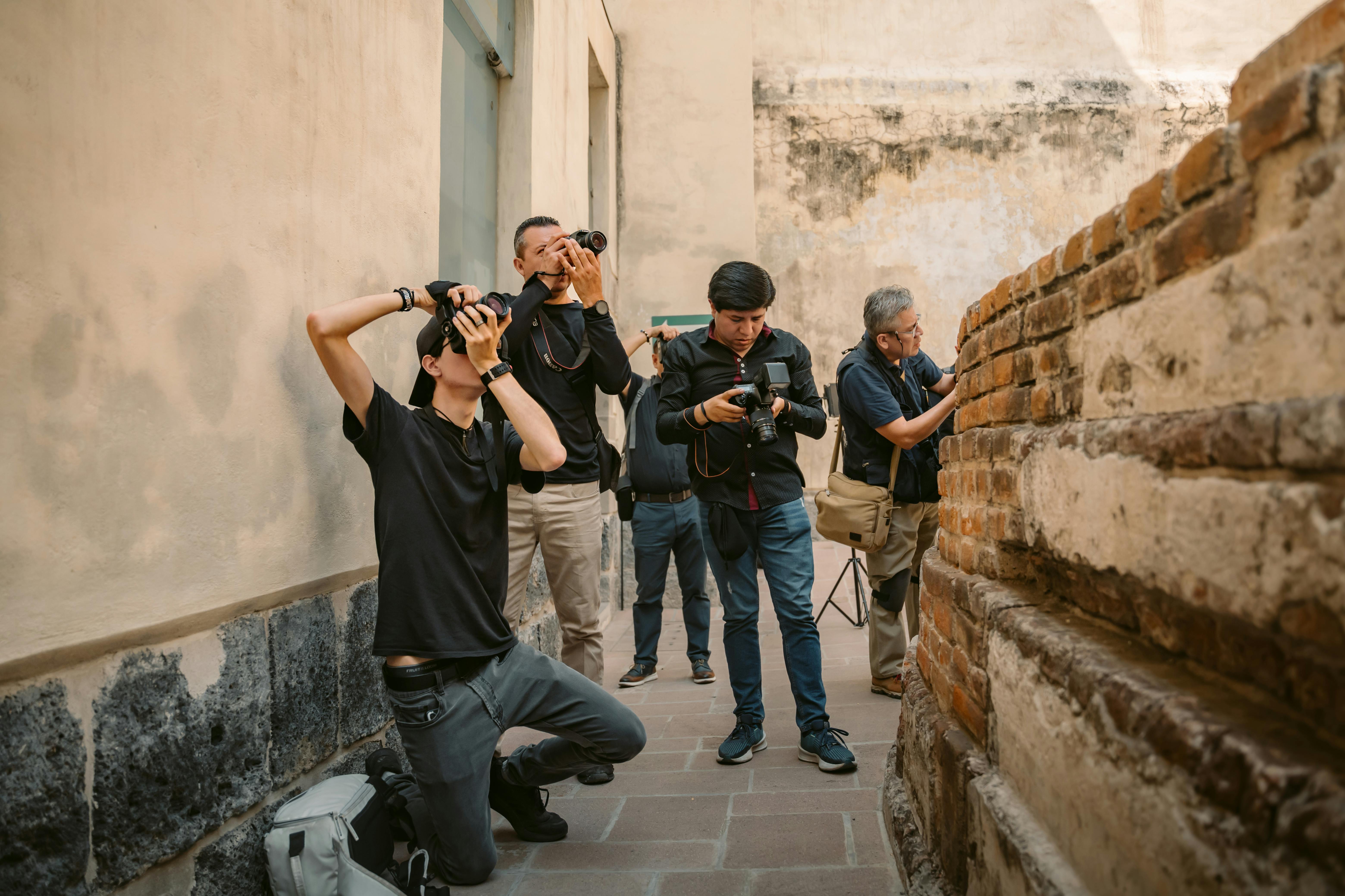 Plusieurs photographes et vidéographes concentrés immortalisent les détails d’un mur ancien dans une ruelle, équipés de matériel professionnel et plongés dans leur passion