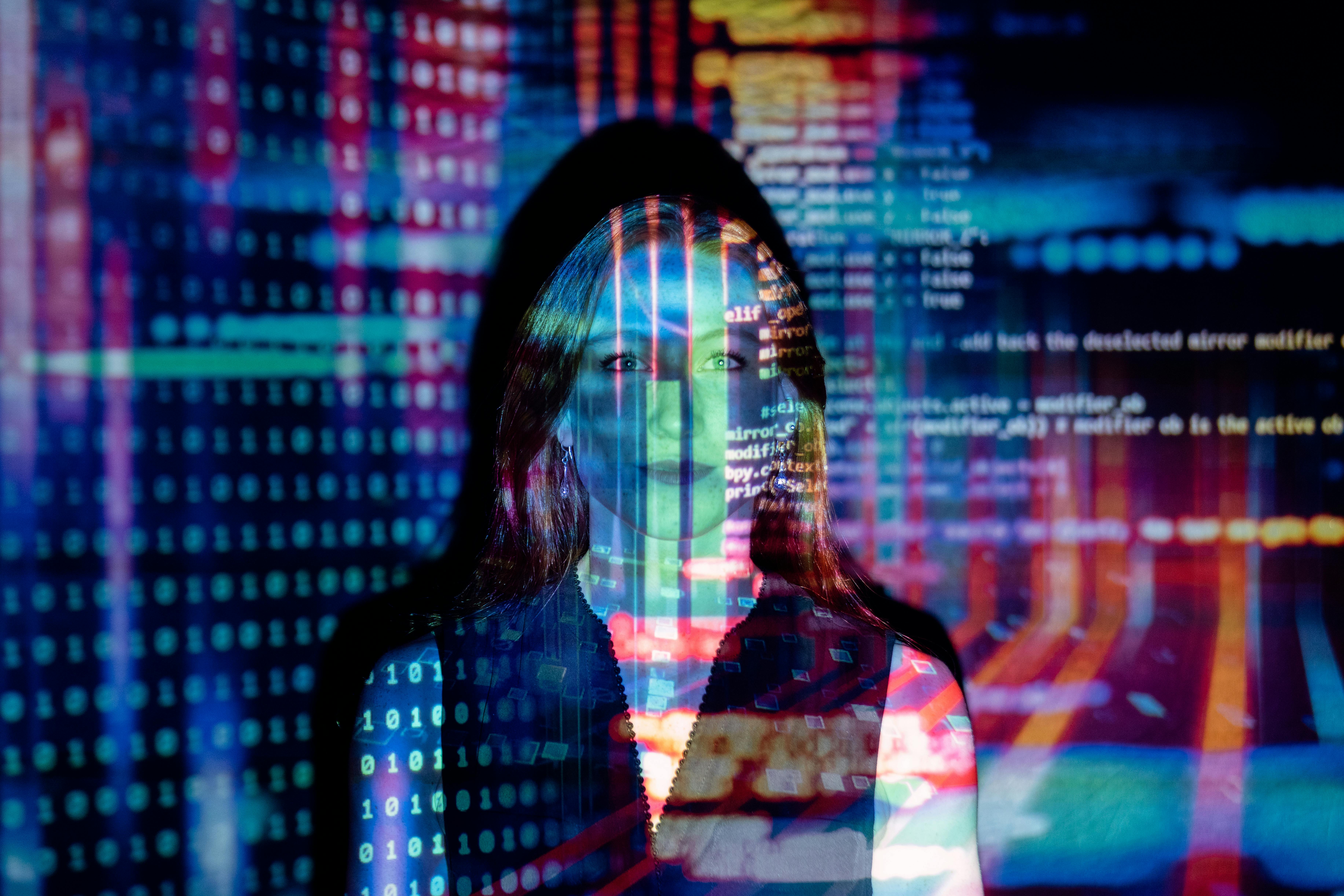 Femme debout dans un environnement numérique, illuminée par des projections de codes sur le mur et sa silhouette