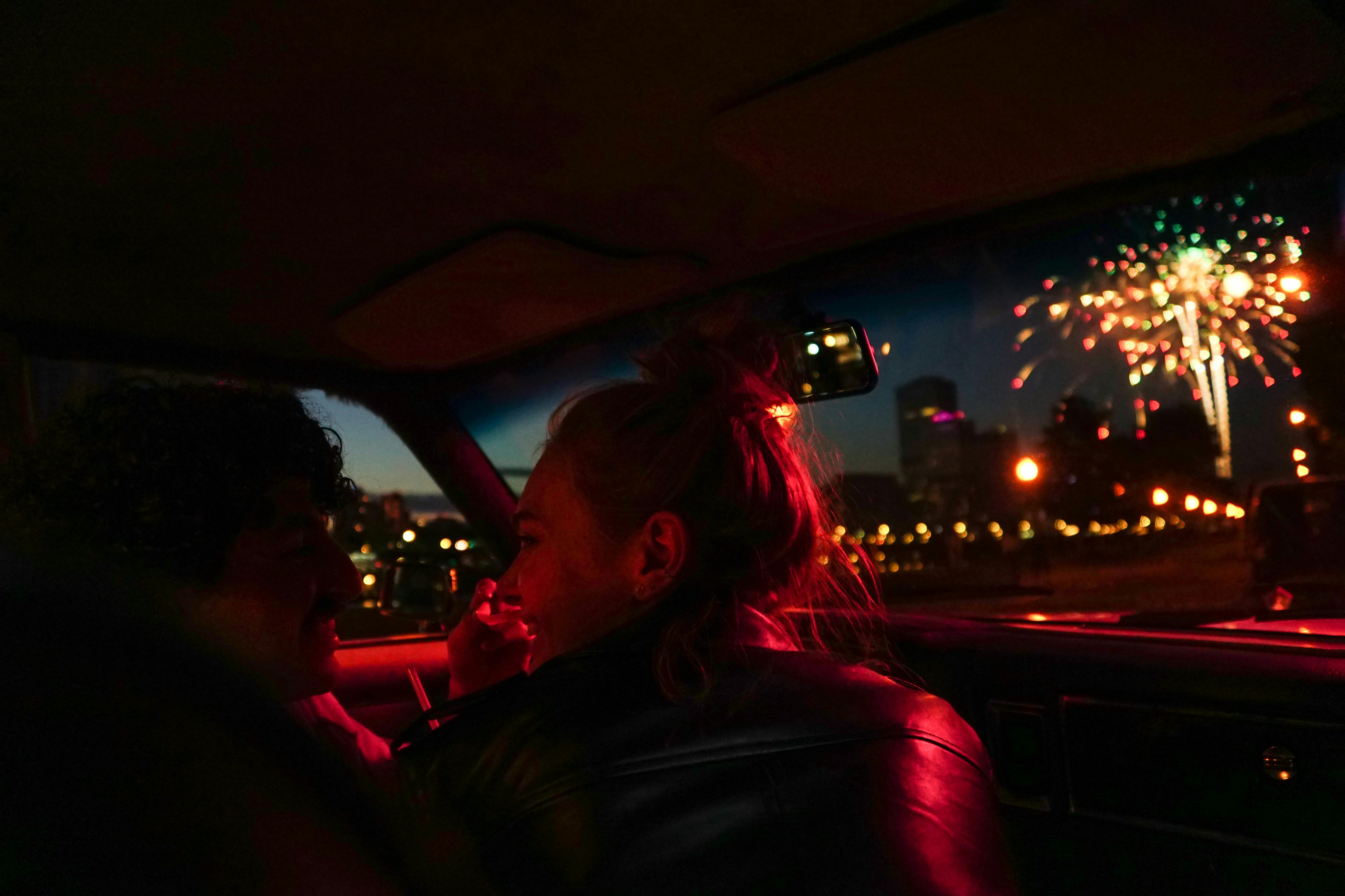 Deux personnes assises dans une voiture avec des feux d'artifice illuminant le ciel en arrière-plan