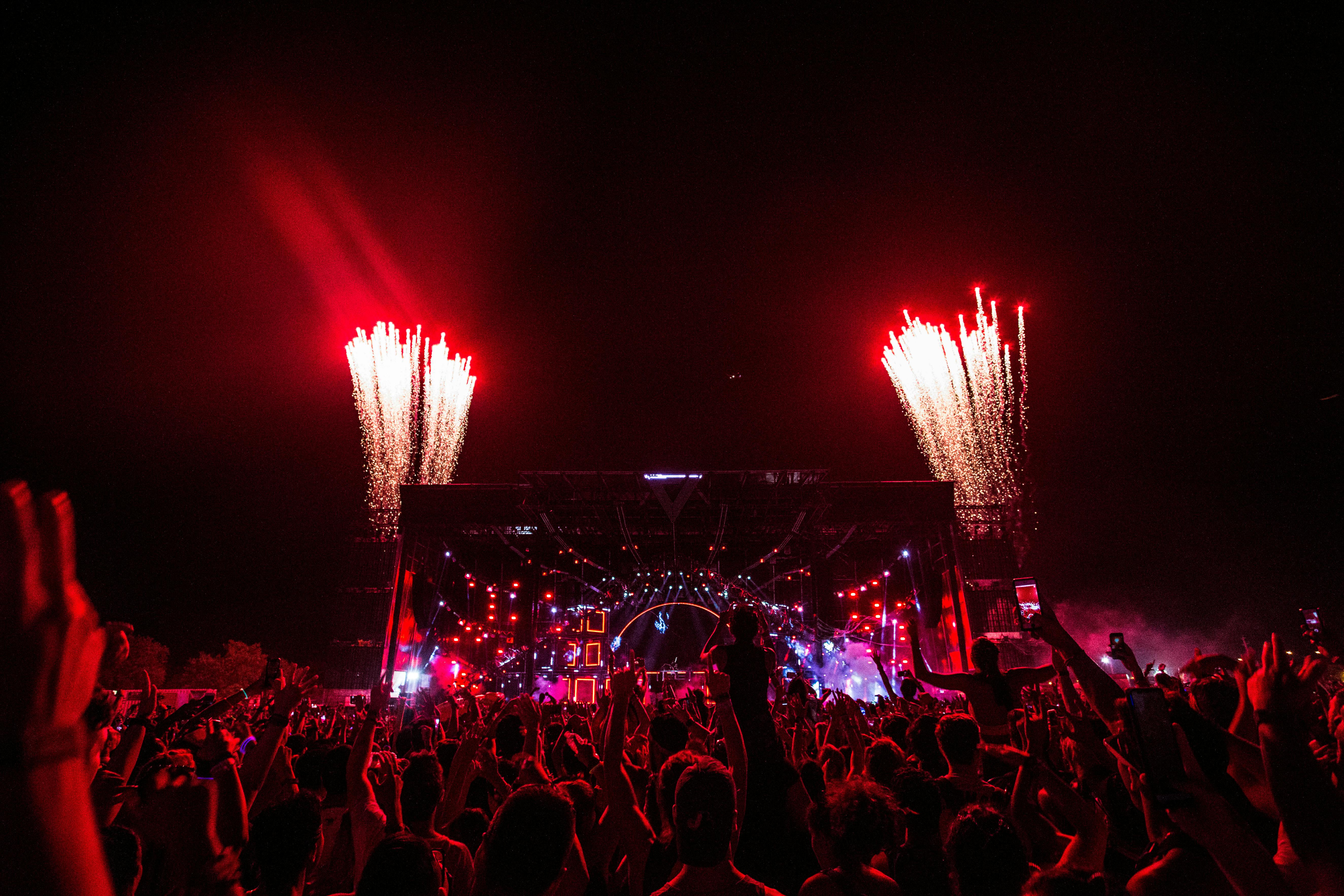 Une foule enthousiaste à un festival de musique, avec des feux d'artifice illuminant le ciel nocturne