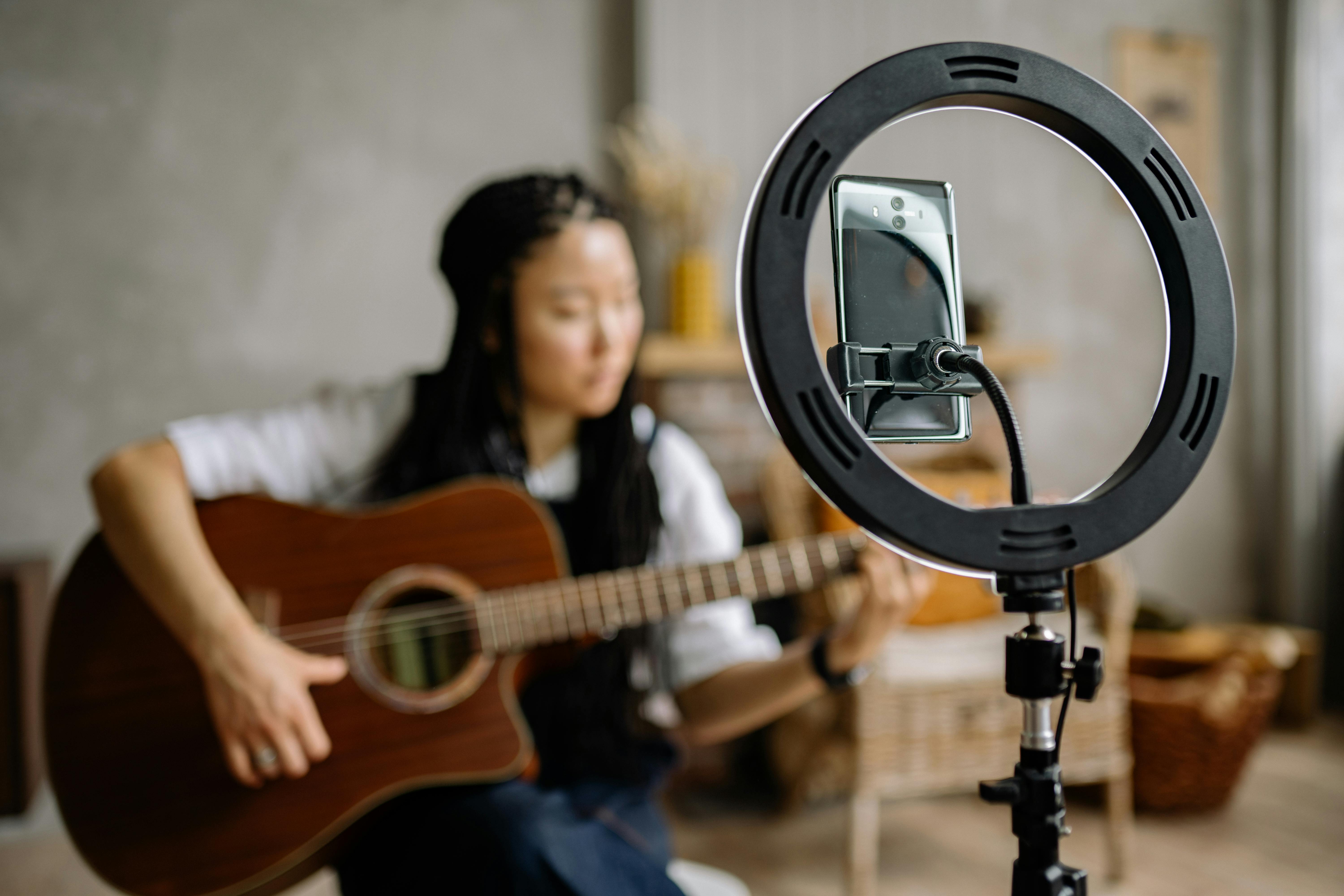 Femme jouant de la guitare sous un anneau lumineux pour selfies, créant une ambiance chaleureuse et artistique