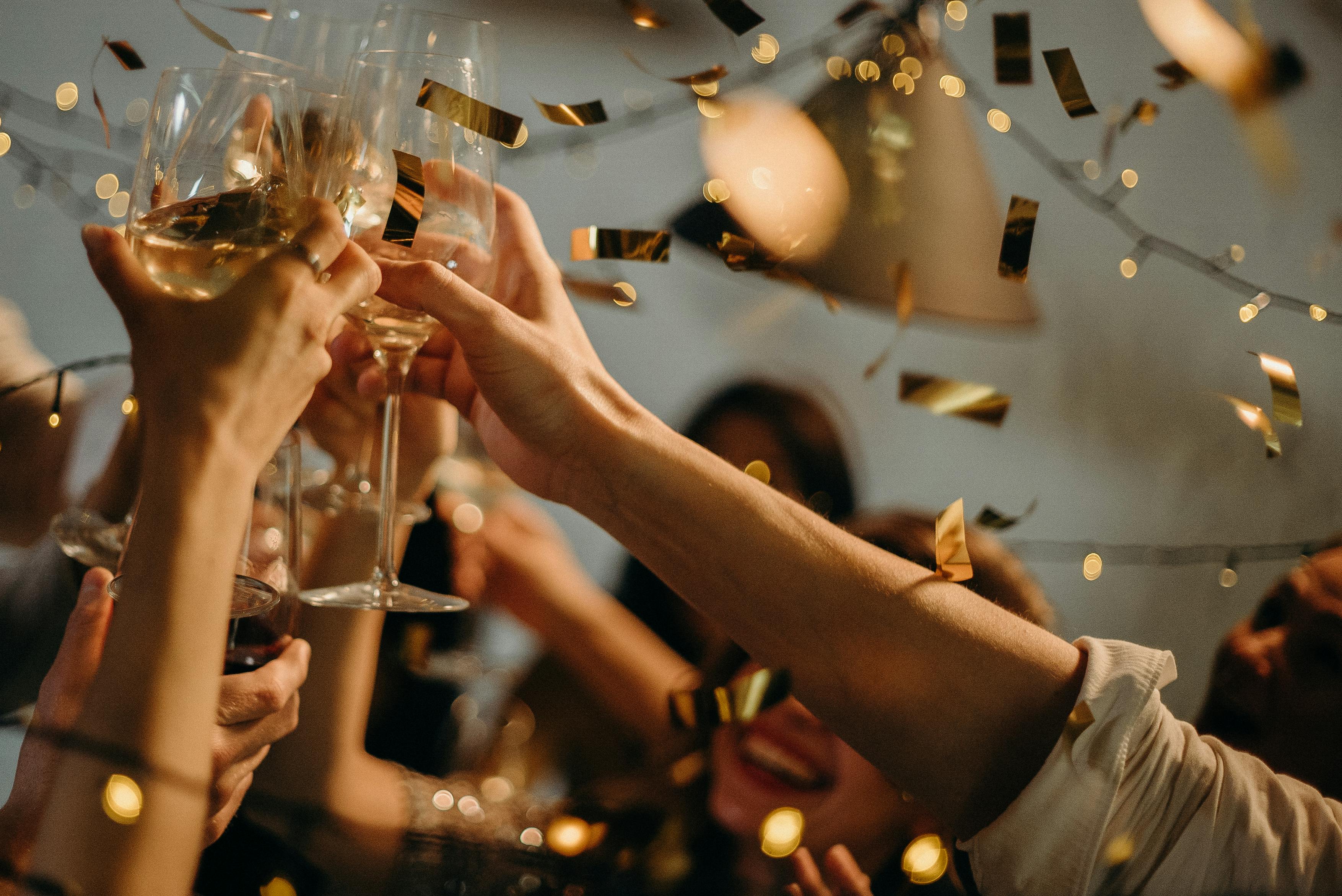 Invités trinquant avec des verres de vin blanc et de champagne sous une pluie de confettis dorés lors d’un mariage festif