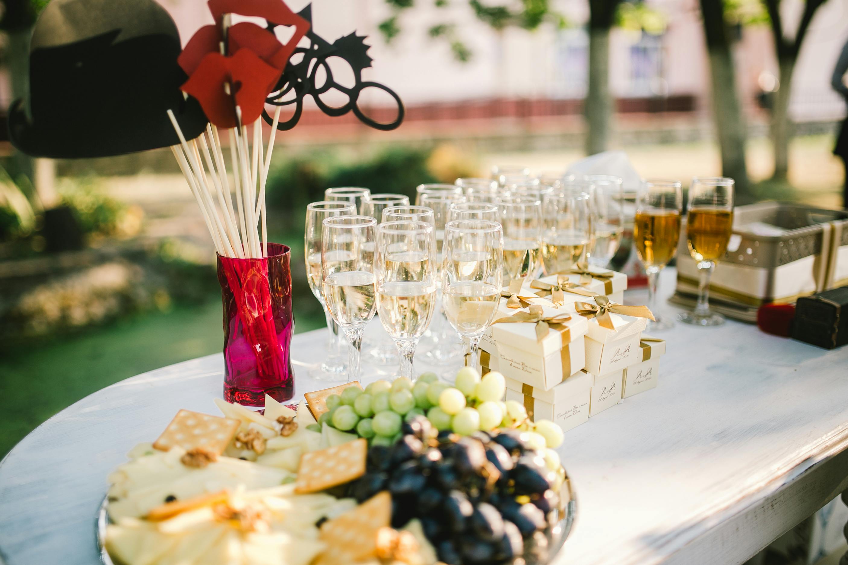 Buffet de mariage en plein air avec verres de vin blanc pétillant, plateaux de fromages et fruits, cadeaux d’invités et décorations ludiques