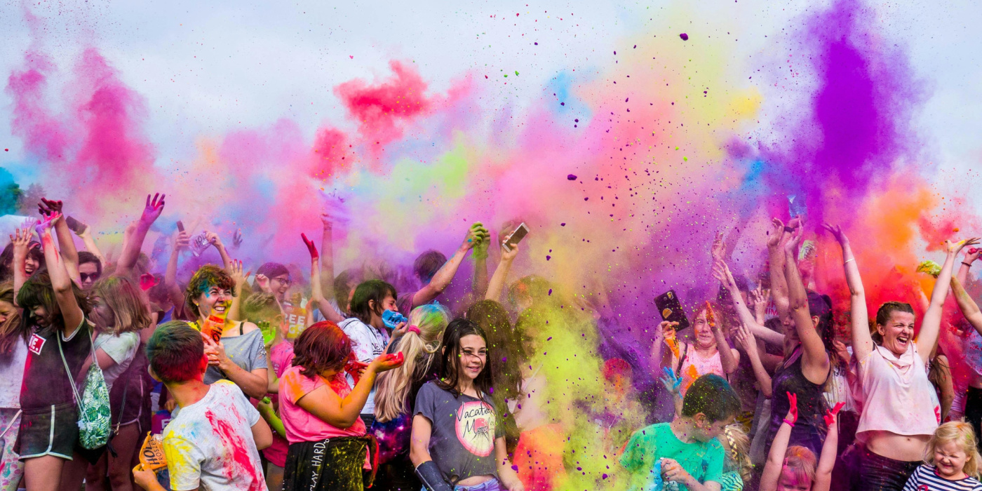 Une foule dynamique en plein air, baignée de fumées colorées et de rires, célèbre dans une ambiance festive et haute en couleur