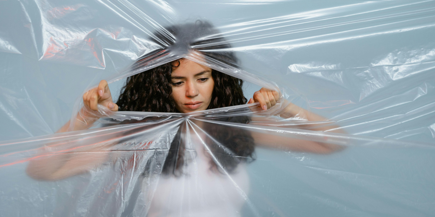 Une femme déchire une bâche transparente devant elle, le regard déterminé et le geste puissant, comme si elle franchissait un cap